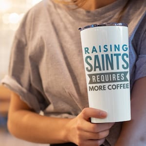 May include: White travel mug with a teal and black design that says "Raising Saints Requires More Coffee".