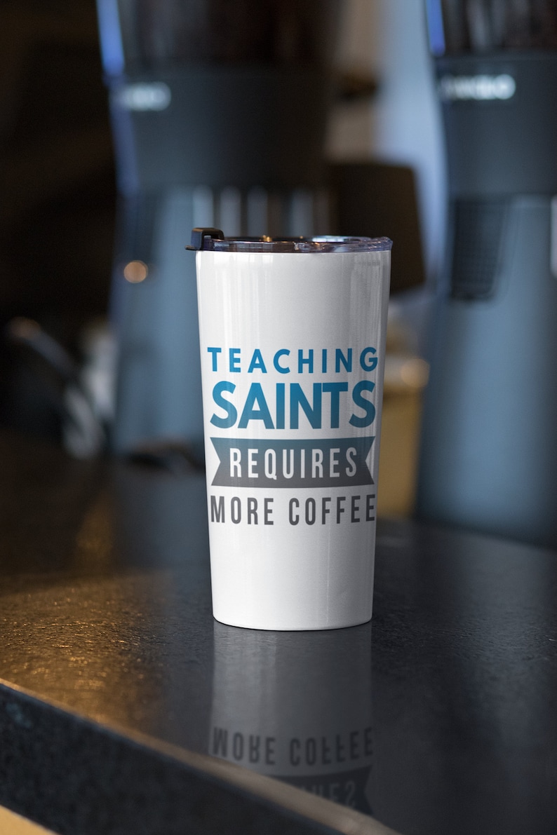 Puede incluir: Taza de viaje blanca con un dise&ntilde;o azul y gris que dice "Ense&ntilde;ar a los santos requiere m&aacute;s caf&eacute;".