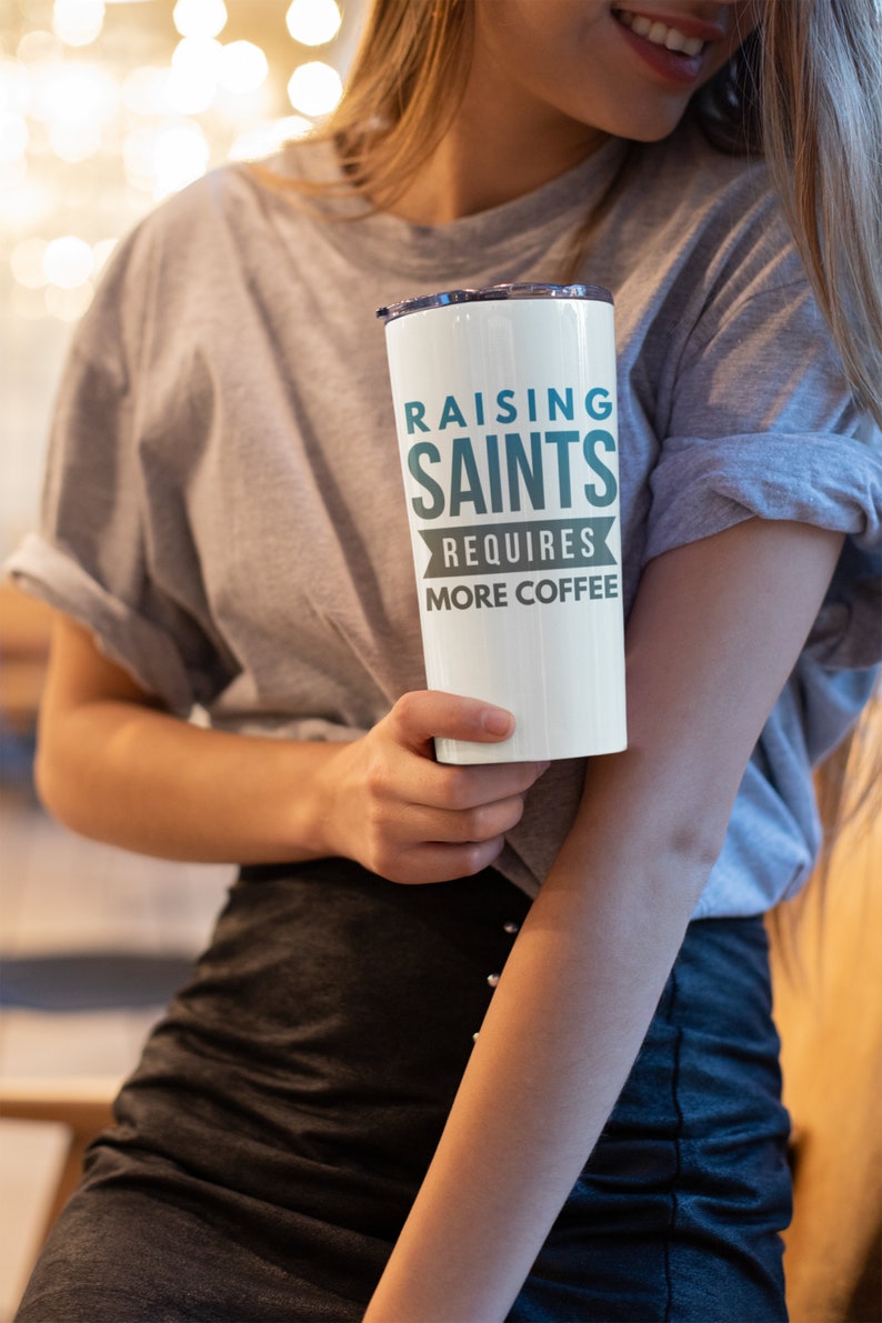 May include: White travel mug with a teal and black design that says "Raising Saints Requires More Coffee".
