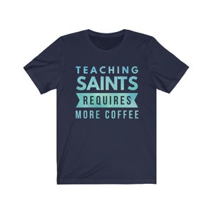 Peut inclure: T-shirt bleu marine avec un design d&eacute;grad&eacute; bleu clair et vert. Le texte "TEACHING SAINTS REQUIRES MORE COFFEE" est imprim&eacute; sur le t-shirt.
