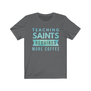 Peut inclure: Un t-shirt gris fonc&eacute; avec un design d&eacute;grad&eacute; bleu et vert. Le texte sur le t-shirt est "Teaching Saints Requires More Coffee".