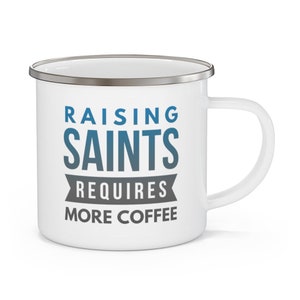 May include: White enamel mug with a silver rim. The mug has a blue and gray graphic that says "Raising Saints Requires More Coffee".