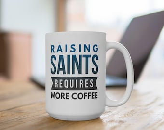 May include: White ceramic coffee mug with the text "Raising Saints Requires More Coffee" in blue and black lettering.