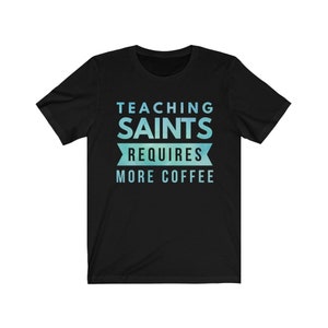 Peut inclure: T-shirt noir avec un design d&eacute;grad&eacute; bleu et vert. Le texte sur le t-shirt est "Teaching Saints Requires More Coffee."