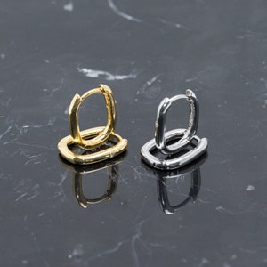 May include: Two pairs of hoop earrings, one gold and one silver, are displayed on a marble surface. The earrings are both square shaped and have a simple design.