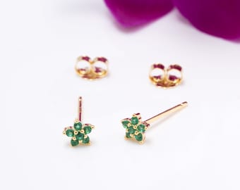 May include: A pair of gold star-shaped earrings with green gemstones. The earrings are on a white background.