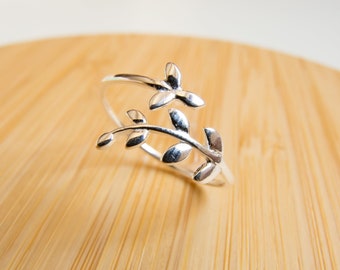 May include: A silver ring with a delicate leaf design. The ring is made of two intertwined branches with leaves.