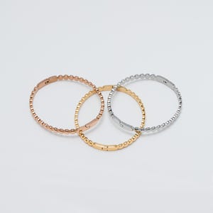 May include: Three beaded bracelets in gold, silver, and rose gold. The bracelets are linked together and are all the same size.