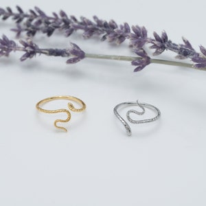 May include: Two snake rings, one gold and one silver, with a textured finish. The rings are on a white background.