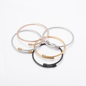 May include: Four different colored metal bracelets with a twisted cable design. The bracelets are stacked on top of each other. The colors are silver, gold, rose gold, and black.