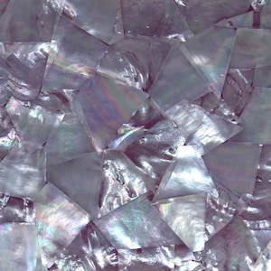 May include: A close-up of a sheet of iridescent mother-of-pearl tiles. The tiles are arranged in a random pattern and have a variety of shapes and sizes. The tiles are a light purple color with a pearlescent sheen.