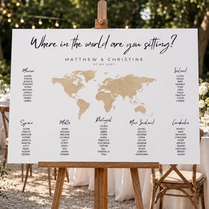 May include: A white rectangular wedding seating chart sign on a wooden easel featuring the text Where in the world are you sitting?, Matthew & Christine, 07.04.2027, a gold world map graphic, and lists of names organized under country headings.