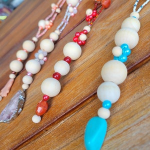 May include: Three necklaces with wooden beads and colorful accents. The necklaces feature different colored beads, including red, pink, turquoise, and white. The necklaces are displayed on a wooden surface.