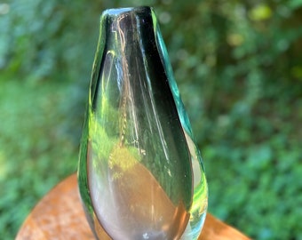 Könnte beinhalten: Eine tropfenförmige Glasvase mit einer klaren, irisierenden Oberfläche. Die Vase hat einen dezenten Grünton und einen abgerundeten Boden.