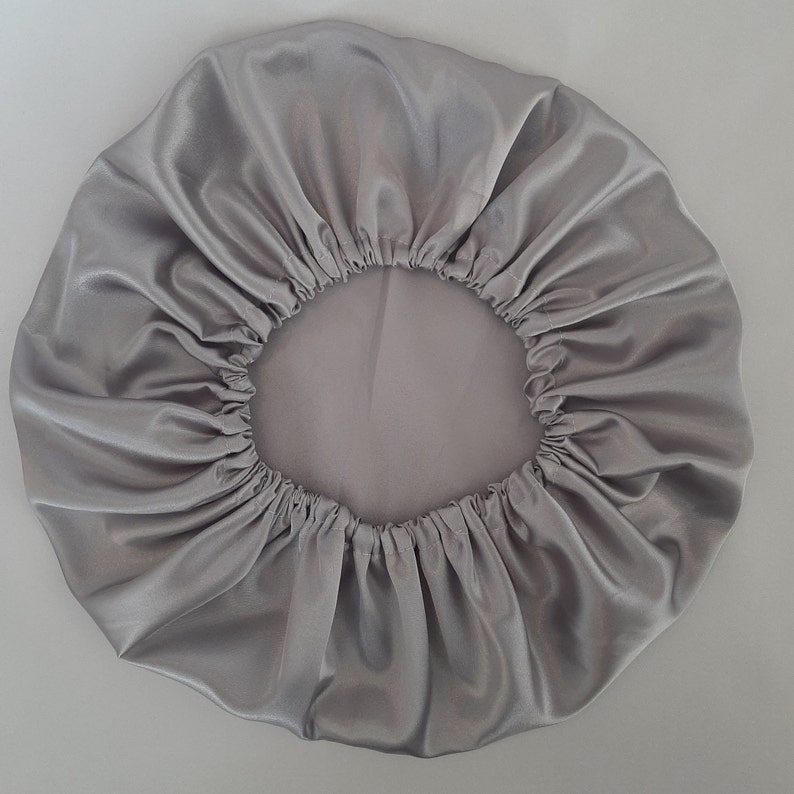 Puede incluir: Un gorro de sat&eacute;n plateado con borde el&aacute;stico. El gorro es redondo y tiene un borde fruncido. La tela tiene un ligero brillo, reflejando la luz. El gorro est&aacute; dise&ntilde;ado para proteger el cabello mientras se duerme.