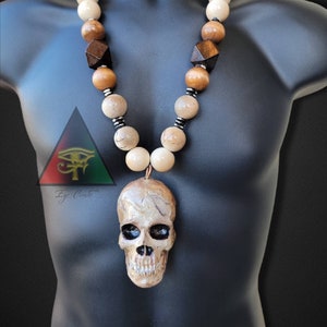 May include: A wooden bead necklace with a skull pendant. The beads are in shades of brown and beige, with some dark brown wooden beads. The skull pendant is made of a light brown material and has black eyes.