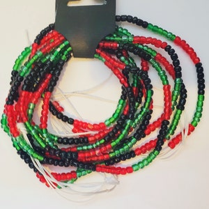 May include: A set of beaded bracelets in red, green, and black colors. The bracelets are made of small, round beads and are strung together in a repeating pattern. The bracelets are tied together with white string.