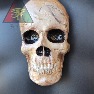 May include: A gold-painted human skull with black eye sockets and a painted smile. The skull is a decorative object.