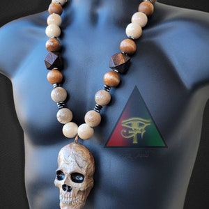 May include: A wooden bead necklace with a skull pendant. The beads are brown, beige, and white. The skull is carved from wood and has a detailed design. The necklace is on a mannequin.