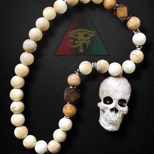 May include: A white and brown beaded necklace with a skull charm. The beads are made of wood and bone. The skull is white with black eyes and a toothy grin. The necklace is hanging on a black background.