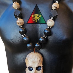 May include: A black and white beaded necklace with a skull pendant. The beads are made of wood and the skull is made of ceramic. The necklace is on a black mannequin.