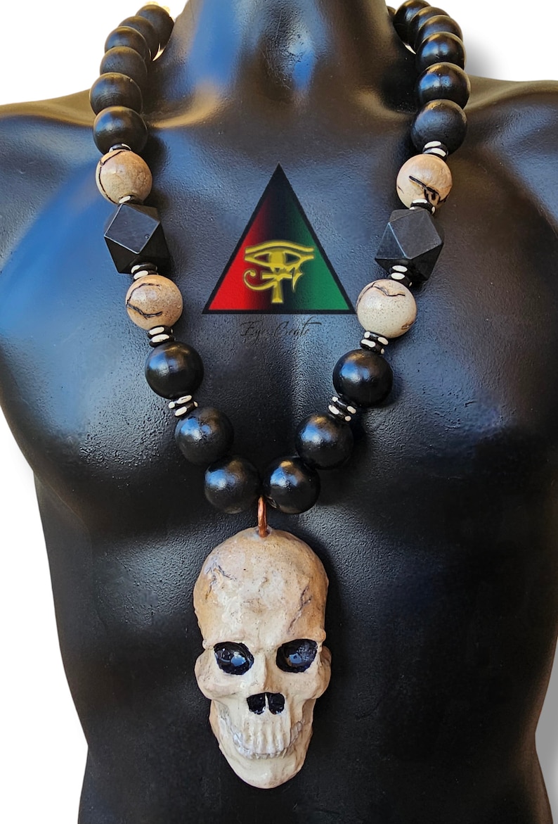 May include: A black and white beaded necklace with a skull pendant. The beads are made of wood and the skull is made of ceramic. The necklace is on a black mannequin.