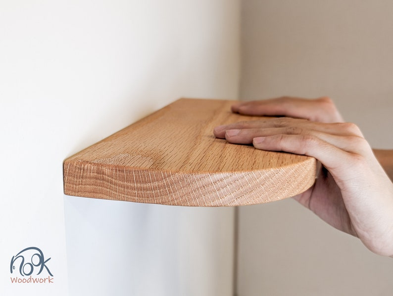 Two hands rest on an oak shelf with rounded corners against the wall