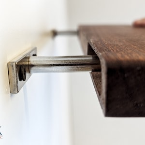 Side view of a mahogany floating shelf fitting into two metal brackets attached to the wall