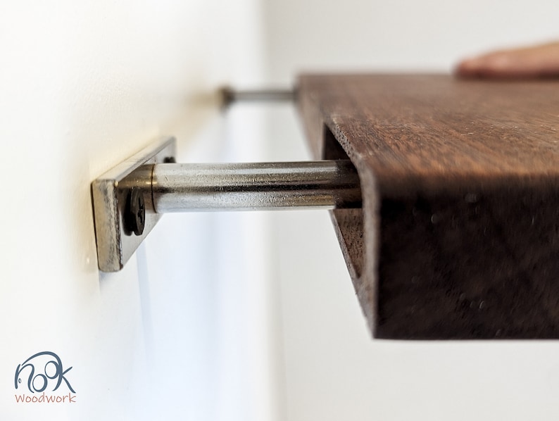 Side view of a mahogany floating shelf fitting into two metal brackets attached to the wall