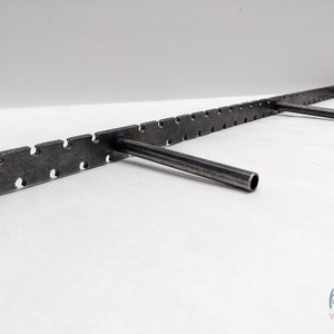 May include: A metal shelf bracket with a long, straight, horizontal bar and three vertical, angled brackets. The horizontal bar has a series of evenly spaced holes and a textured surface.