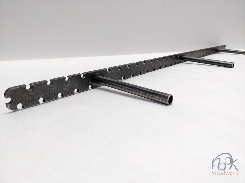 May include: A metal shelf bracket with a long, straight, horizontal bar and three vertical, angled brackets. The horizontal bar has a series of evenly spaced holes and a textured surface.