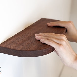 Two hands rest on a mahogany floating shelf with curved corners