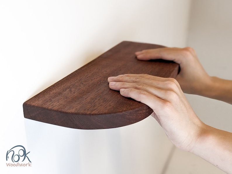 Two hands rest on a mahogany floating shelf with curved corners