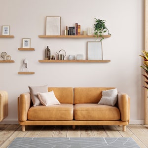 Two hands grip the top and bottom of the front piece of a long wooden oak shelf and easily install it onto the wall by sliding the shelf onto black brackets.