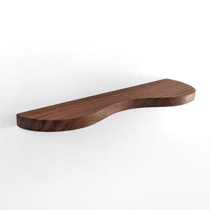 Puede incluir: Una estantería de madera curvada hecha de madera de nogal. La estantería está montada en una pared blanca.