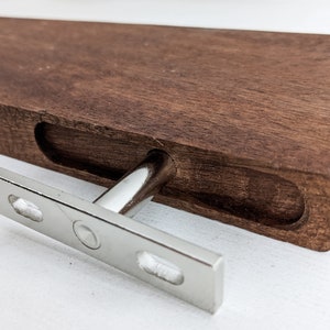 Pu&ograve; includere: Un supporto per mensola in legno con un supporto a T in metallo argentato. Il supporto &egrave; in legno marrone scuro e ha una finitura liscia. Il supporto metallico &egrave; fissato al supporto con viti.