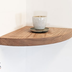 A candle is displayed on top of an oak corner floating shelf with a rounded front face.