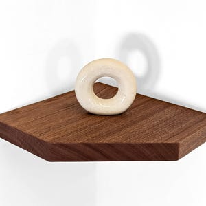 Front view of a mahogany floating shelf displaying a donut sculpture.