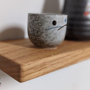 Pu&ograve; includere: Un piccolo ripiano in legno marrone chiaro con un bordo arrotondato. Una tazza in ceramica grigia con disegni neri e blu si trova sullo scaffale.
