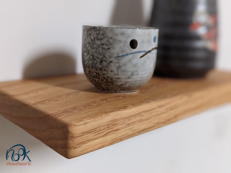 Pu&ograve; includere: Un piccolo ripiano in legno marrone chiaro con un bordo arrotondato. Una tazza in ceramica grigia con disegni neri e blu si trova sullo scaffale.