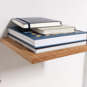 Pu&ograve; includere: Una pila di libri su uno scaffale di legno. Il libro in cima &egrave; un quaderno blu scuro con una spina dorsale bianca. Il secondo libro &egrave; un quaderno bianco con una spina dorsale blu. Il libro in fondo &egrave; un libro rilegato blu con una spina dorsale bianca. Lo scaffale &egrave; fatto di legno marrone chiaro.