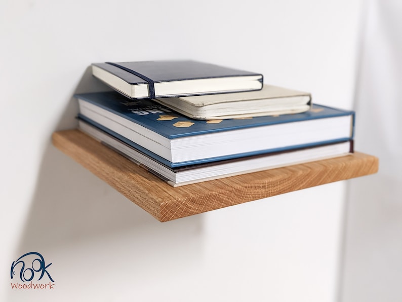 Pu&ograve; includere: Una pila di libri su uno scaffale di legno. Il libro in cima &egrave; un quaderno blu scuro con una spina dorsale bianca. Il secondo libro &egrave; un quaderno bianco con una spina dorsale blu. Il libro in fondo &egrave; un libro rilegato blu con una spina dorsale bianca. Lo scaffale &egrave; fatto di legno marrone chiaro.