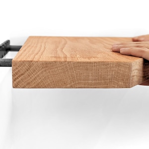Side view of two hands pushing an oak floating shelf onto its bracket