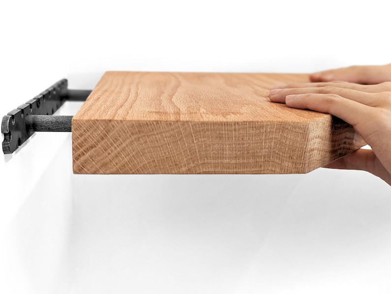 Side view of two hands pushing an oak floating shelf onto its bracket
