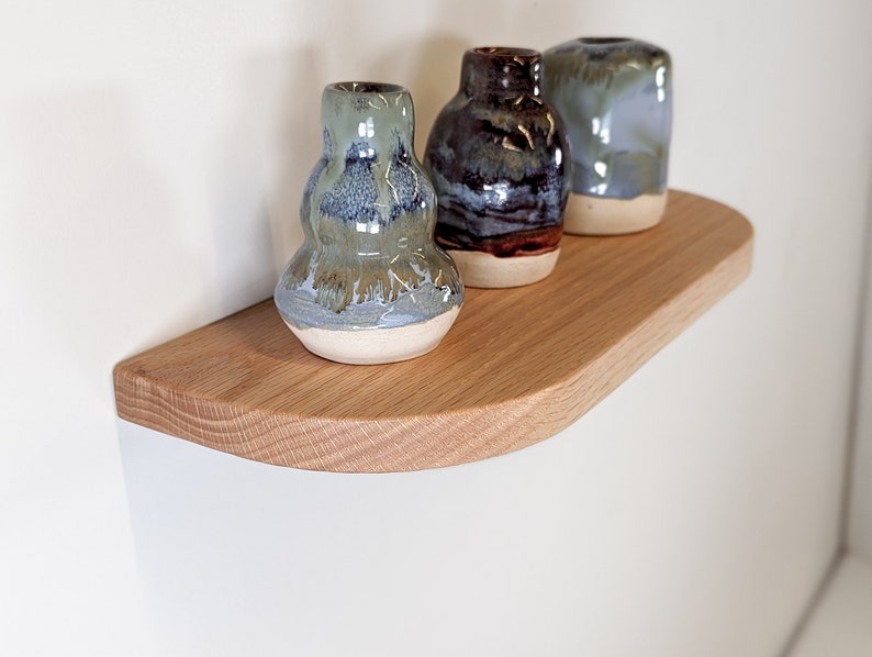 Angled view of a thin oak floating shelf with rounded corners and three vases resting on top
