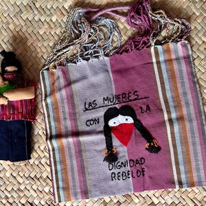 May include: A pink and white striped tote bag with a black and red embroidered image of a woman with the text "Las mujeres con la dignidad rebelde".
