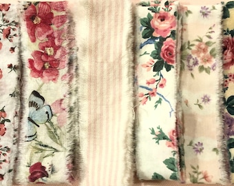 May include: Six strips of fabric with floral patterns, including pink roses, butterflies, and small flowers. The fabric is a light cream color with a slightly textured surface.