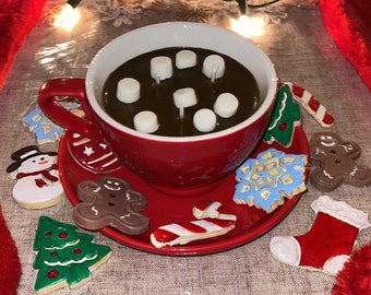 Könnte beinhalten: Eine rote Keramiktasse gefüllt mit heißer Schokolade und Marshmallows, umgeben von Weihnachtskeksen, darunter ein Schneemann, ein Lebkuchenmann und ein Weihnachtsbaum.