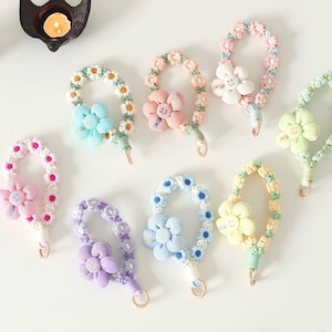 May include: Assortment of colorful daisy flower keychain charms with a smiley face on each flower. The keychains are made of a soft, crocheted material and have a gold-colored metal ring.