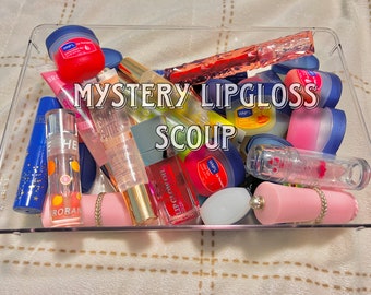 May include: A clear plastic container filled with a variety of lip glosses and lip balms. The container is labeled "MYSTERY LIPGLOSS SCOUP".